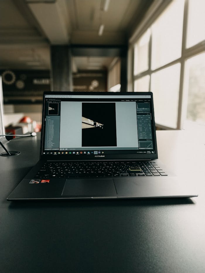 Laptop with photo editing software open on a desk in an office setting, showcasing a modern workspace.